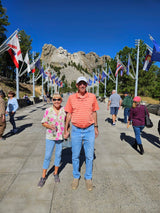 Happy couple holds hands at iconic Mount Rushmore, flanked by flags. A perfect destination for an RV rental trip!