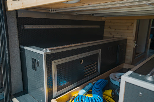 Organized RV rental utility bay with custom-built storage, power outlets, and an open drawer for tools.