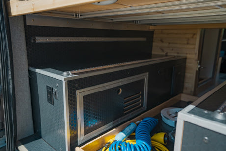 Organized RV rental utility bay with custom-built storage, power outlets, and an open drawer for tools.