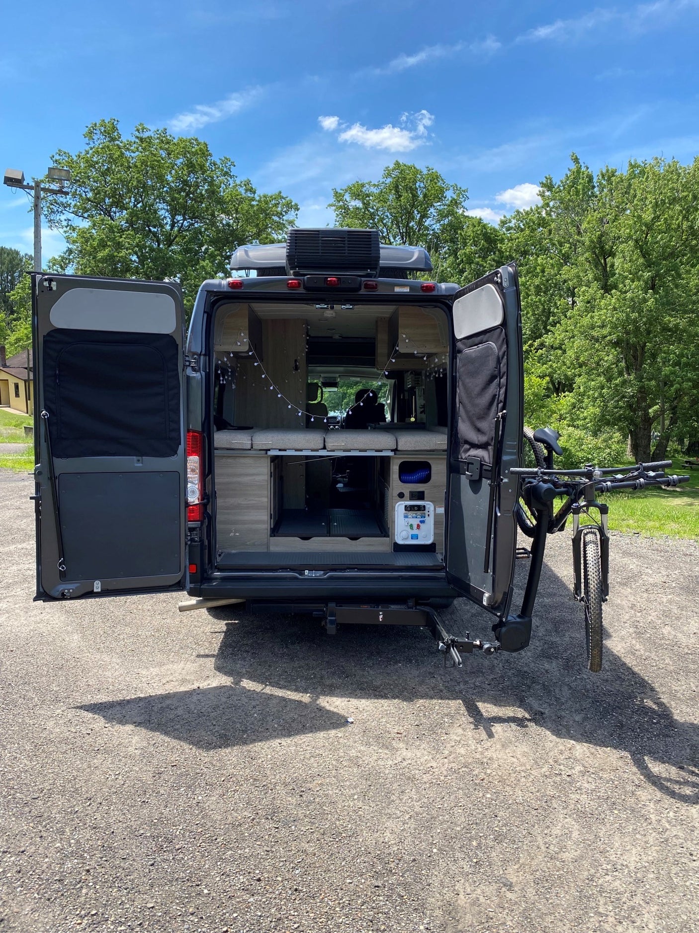 This **RV rental** showcases its open rear doors revealing a custom interior, power station, and bike rack with a mountain bike.