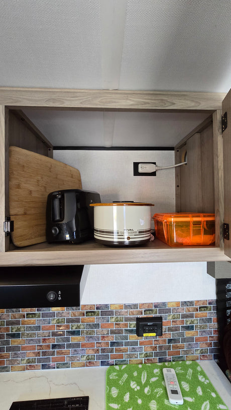 Upper cabinet in an **rv rental** kitchen holds a toaster, slow cooker, and cutting board. Below, a range hood and tiled backsplash.