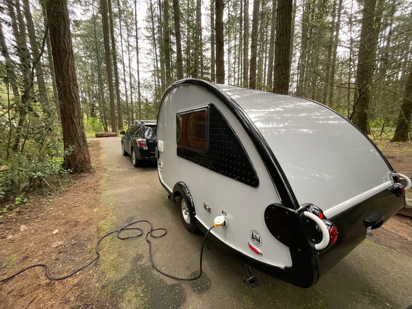  hitched to a car. Ideal for outdoor adventures.|Teardrop RV rental parked in a peaceful forested campground