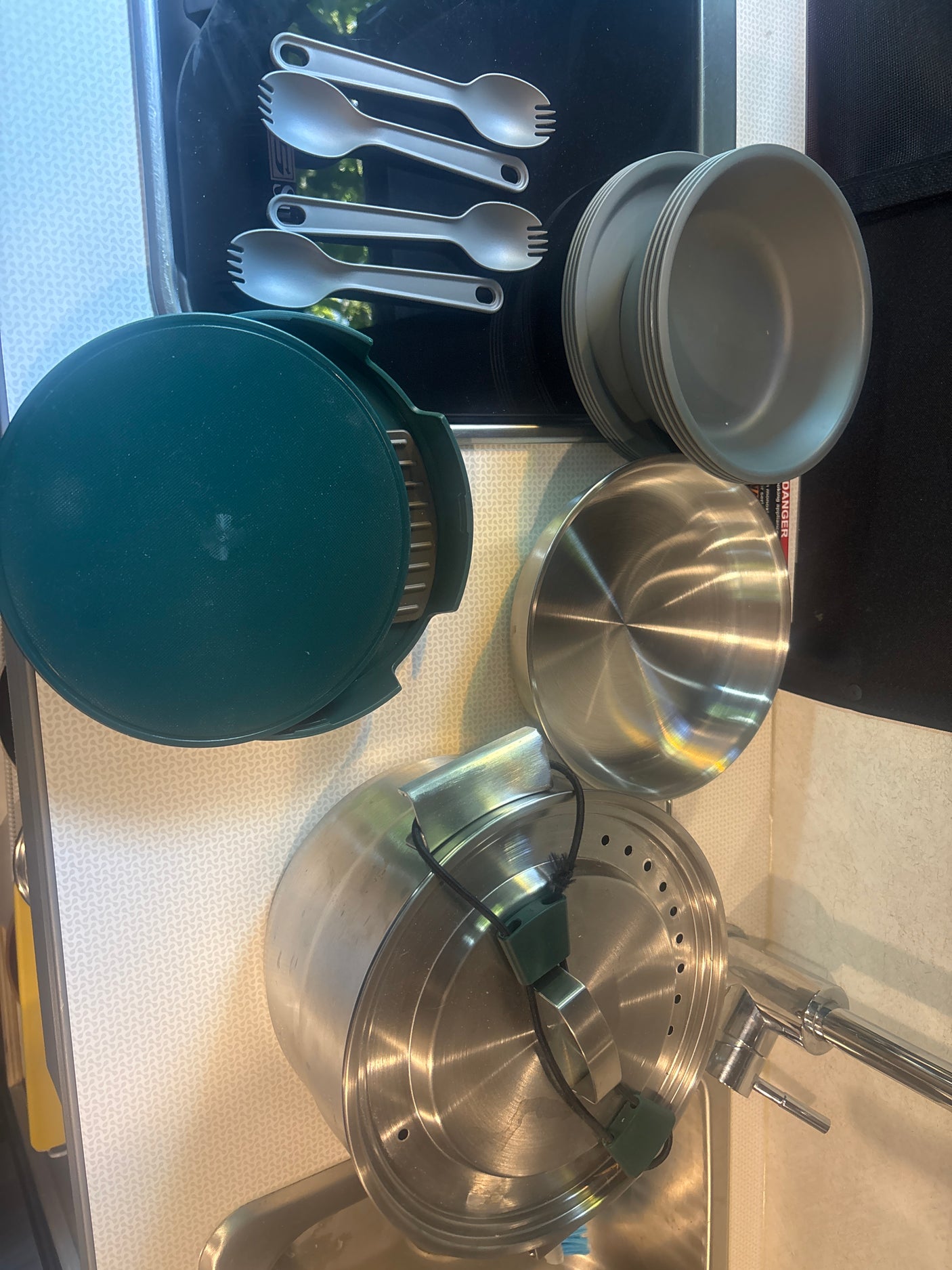 RV rental kitchenware: plastic sporks, bowls, dark green pan, & stainless steel pots for space-saving meals.