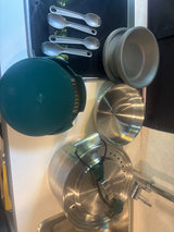 RV rental kitchenware: plastic sporks, bowls, dark green pan, & stainless steel pots for space-saving meals.