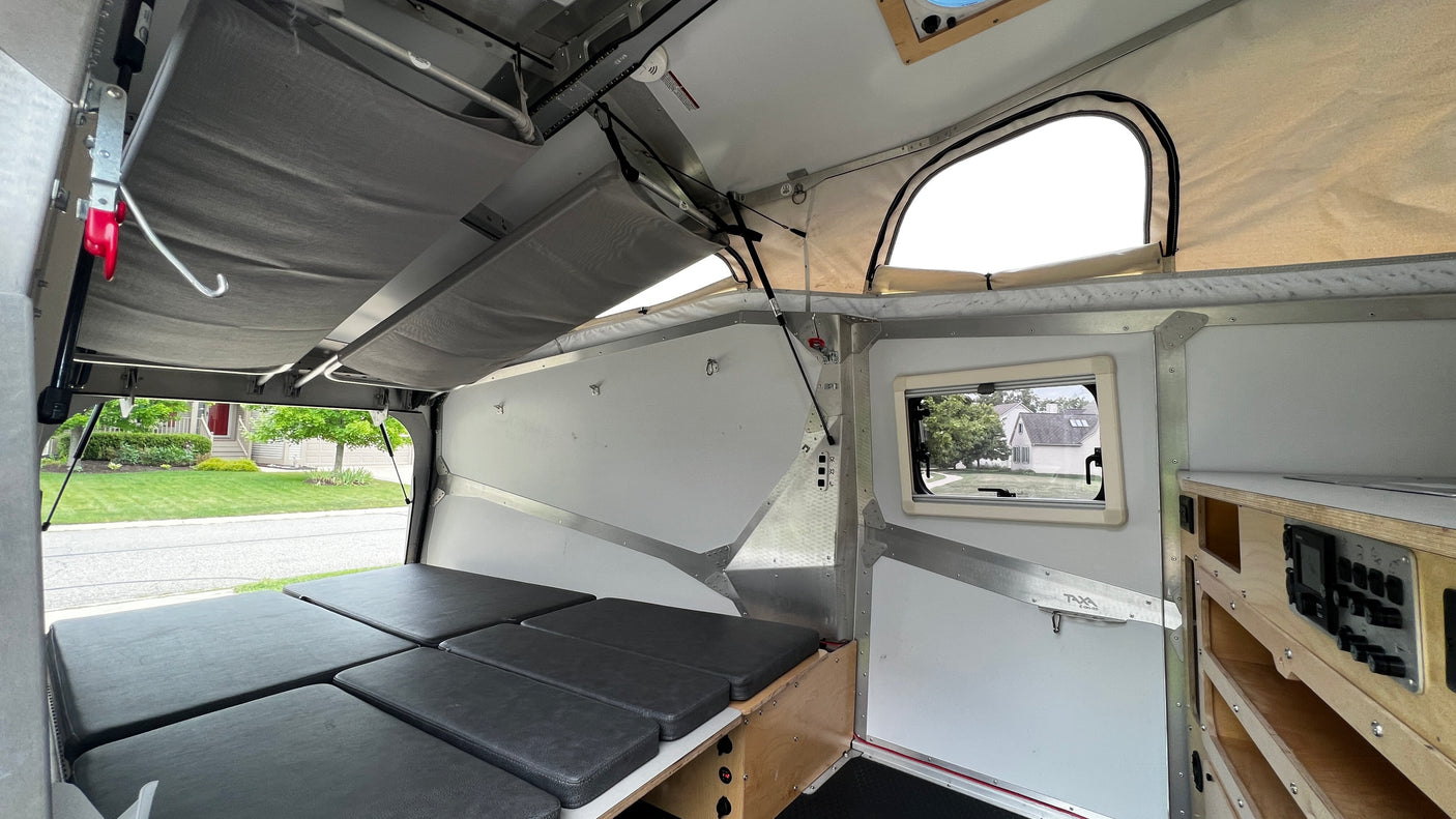 Compact RV rental interior featuring a convertible bed, pop-up roof, and organized controls. Ideal for outdoor adventures.