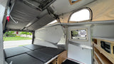 Compact RV rental interior featuring a convertible bed, pop-up roof, and organized controls. Ideal for outdoor adventures.