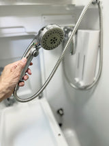 Inside an **rv rental**: a hand holds a compact showerhead & hose in a functional, white wet-bath.