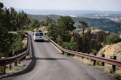 RV rental on a winding mountain road, with guardrails, trees, and scenic cliff views. Perfect road trip!