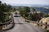 RV rental on a winding mountain road, with guardrails, trees, and scenic cliff views. Perfect road trip!
