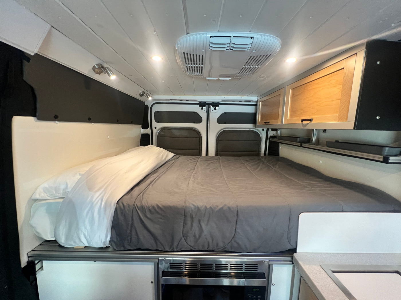 This cozy RV rental interior features a queen-sized bed, overhead storage cabinets, and a convenient under-bed microwave. — photo 6