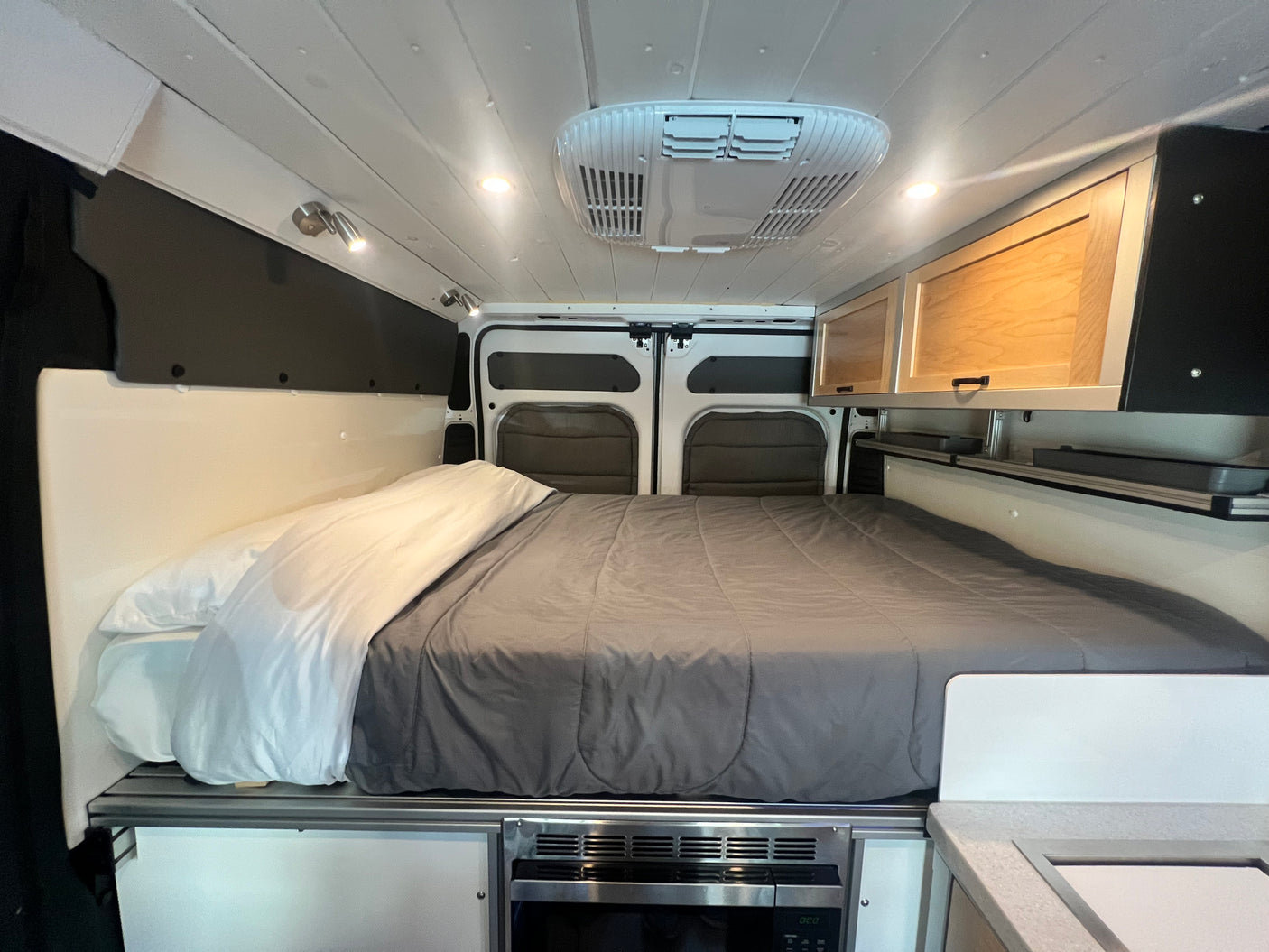 This cozy RV rental interior features a queen-sized bed, overhead storage cabinets, and a convenient under-bed microwave.