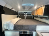 This cozy RV rental interior features a queen-sized bed, overhead storage cabinets, and a convenient under-bed microwave.