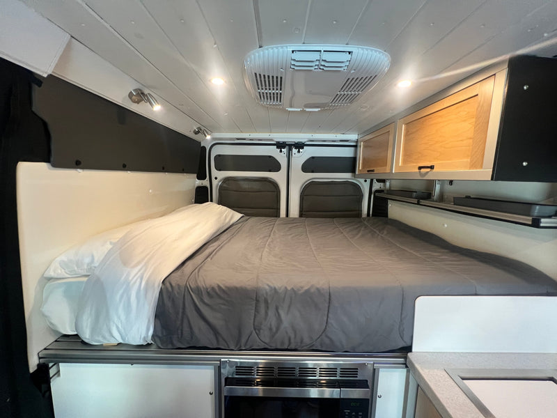 This cozy RV rental interior features a queen-sized bed, overhead storage cabinets, and a convenient under-bed microwave. — photo 6