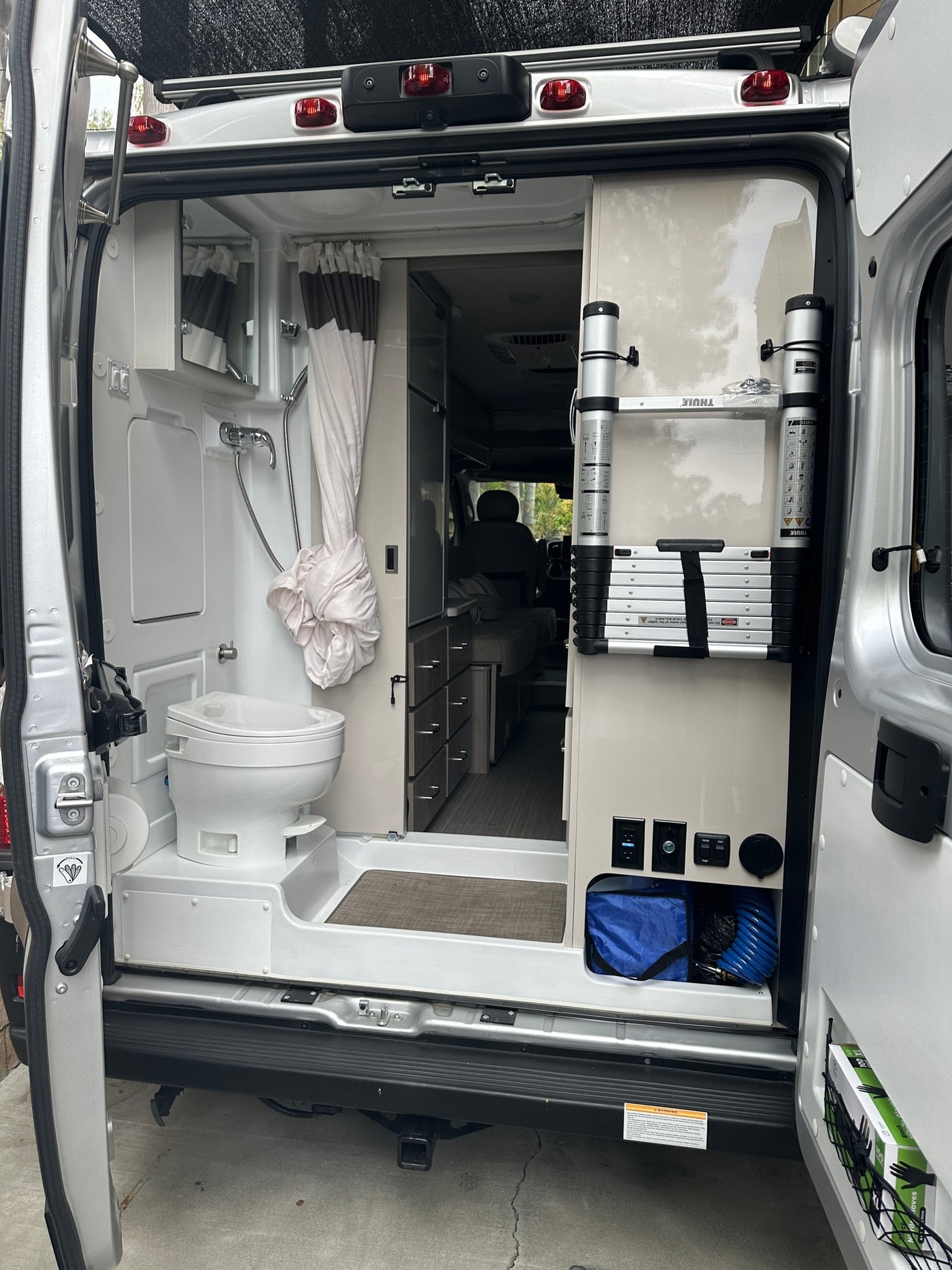 Explore this rv rental's interior. A camper van's rear shows a wet bath (toilet, shower) & storage with a Thule ladder. — photo 9
