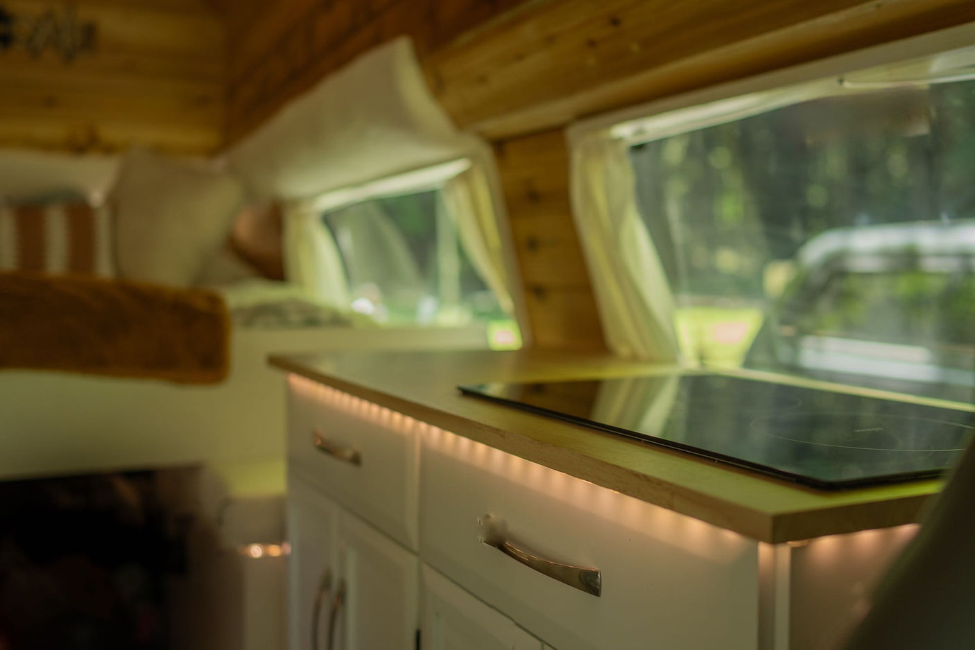 Cozy rv rental interior: A modern kitchen with induction cooktop, bright under-cabinet lighting, and white cabinets.