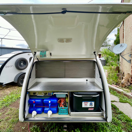 RV rental teardrop camper galley, featuring a compact kitchen with water tanks and a cooler for camping.