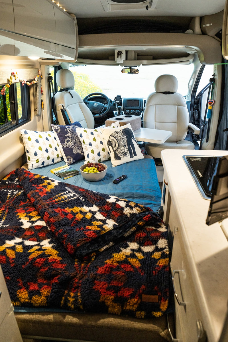 Step inside a comfortable RV rental: modern camper van interior with cozy bed, stylish pillows, and front cabin access. — photo 10