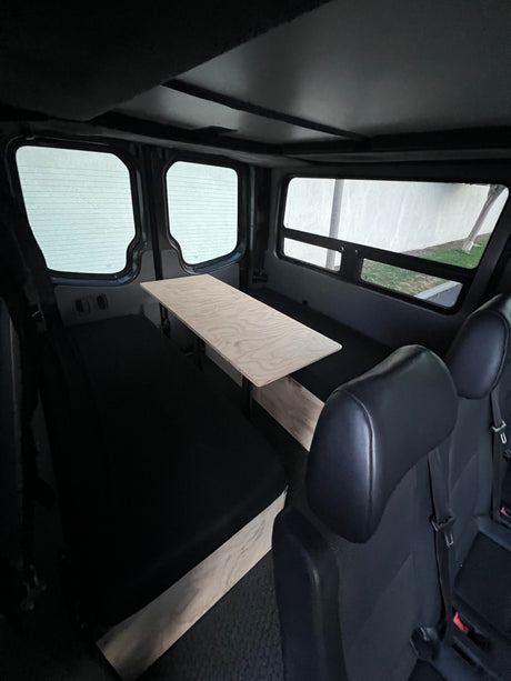 This RV rental features a functional interior with a light wood table, black padded benches, and large windows.