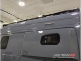 Side view of a grey RV rental, featuring a roof rack, small windows, and an exterior LED light.