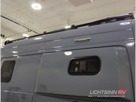 Side view of a grey RV rental, featuring a roof rack, small windows, and an exterior LED light.