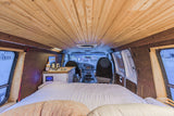 Cozy rv rental camper van interior with wood paneling, bed, small kitchen, and front cab view. Ideal for van life adventures.