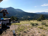 RV rental adventure: cooking outdoors with propane stove, amidst serene mountains and lush forests. Ideal camping setup.