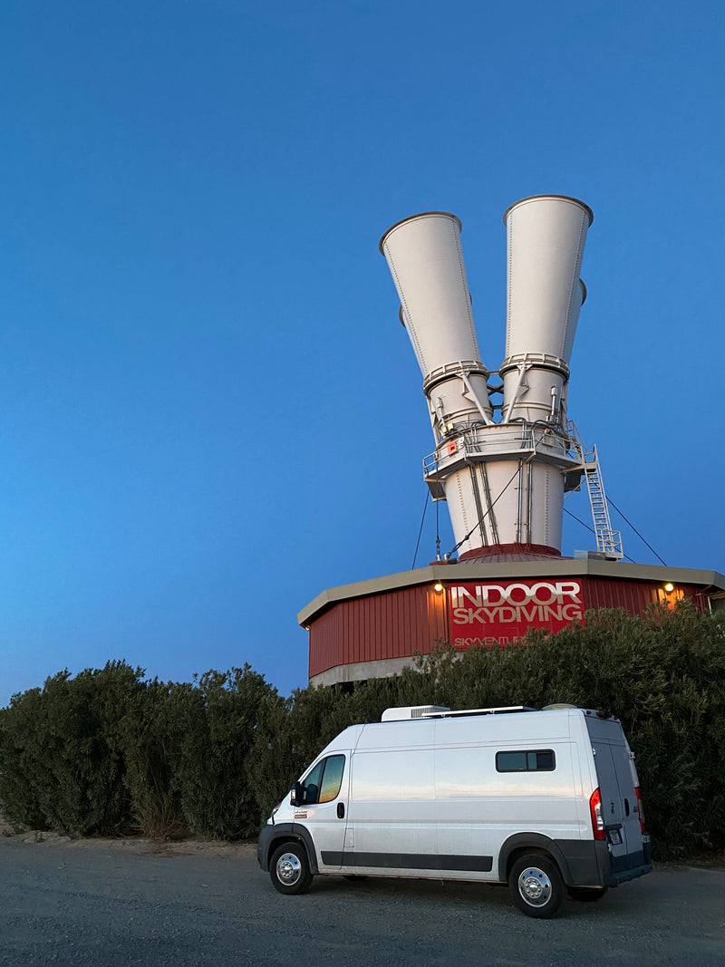 An RV rental camper van parked at an Indoor Skydiving facility with wind tunnels and 'SkyVenture' sign under a clear blue sky. — photo 11