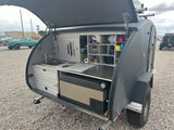 Compact RV rental: Teardrop trailer's organized outdoor kitchen with sink, fridge, and storage, perfect for camping adventures.