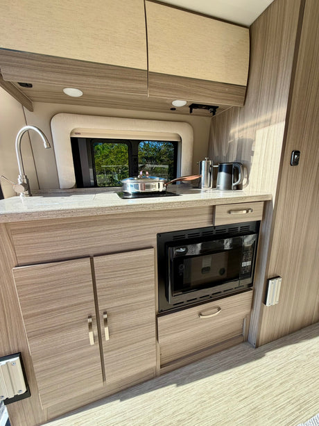 Compact RV rental kitchen with sink, microwave, and stovetop, perfect for travel cooking.