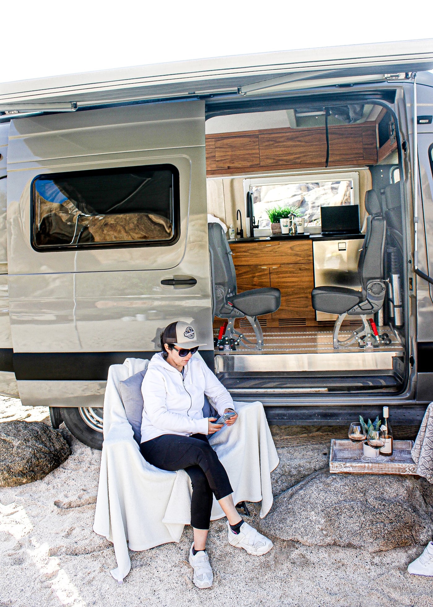 A woman relaxes in a chair outside a modern RV rental van, showcasing its open interior with a kitchenette and comfortable seating. — photo 6