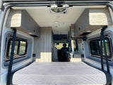 Spacious RV rental interior with a comfortable bed, side windows, overhead storage, and a full kitchen.
