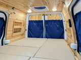 Cozy wood-paneled RV rental campervan interior features a comfy bed, privacy curtains, and open shelving.