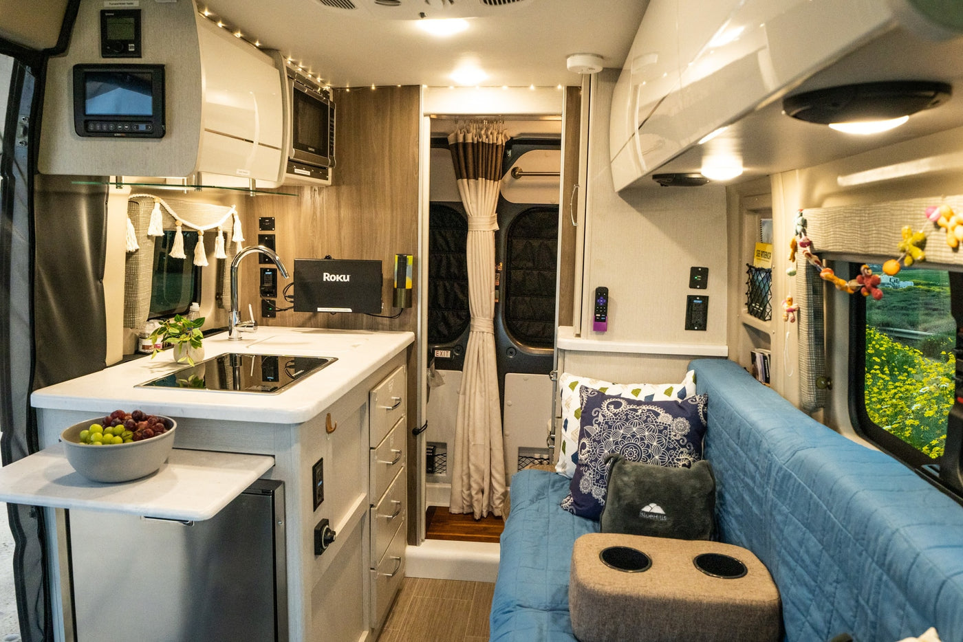 Cozy rv rental interior with a functional kitchenette, comfy seating, and scenic window views of yellow flowers, ideal for travel. — photo 2