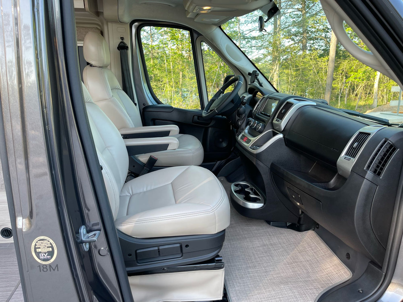 Inside an rv rental: inviting front cabin with comfortable beige seats, modern dashboard, and a view of green trees. — photo 5