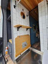 Modern RV rental interior: tiled shower wall, folding table, wooden ceiling & floor, compact living space.