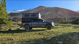 Grey Ford Raptor truck with pop-top camper parked in mountains for off-grid overlanding. Perfect RV rental adventure!