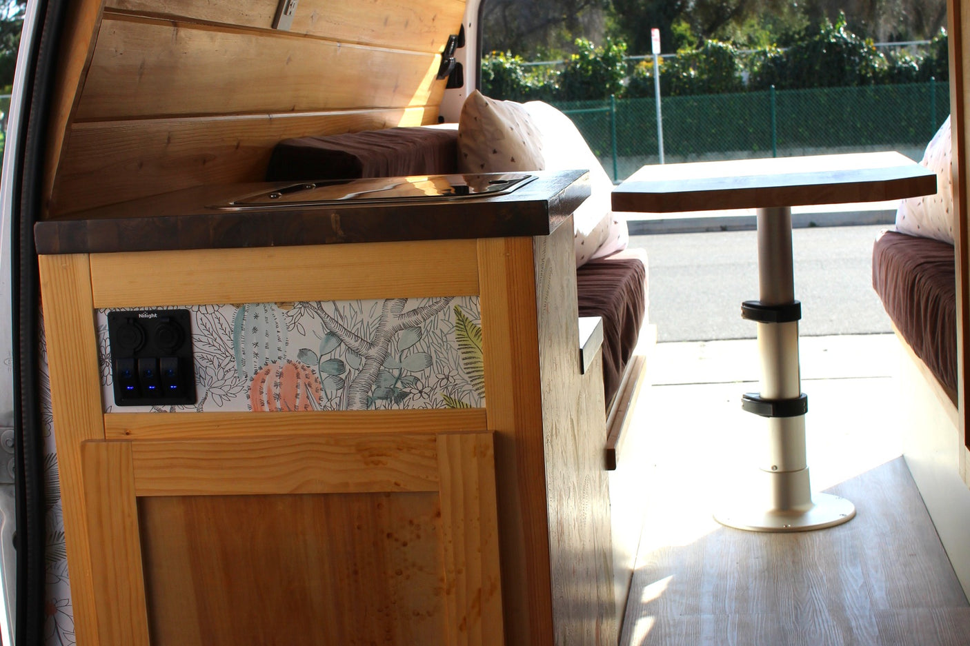 RV rental interior: custom wood kitchen, patterned wall, and flexible table setup for compact living in this camper van.