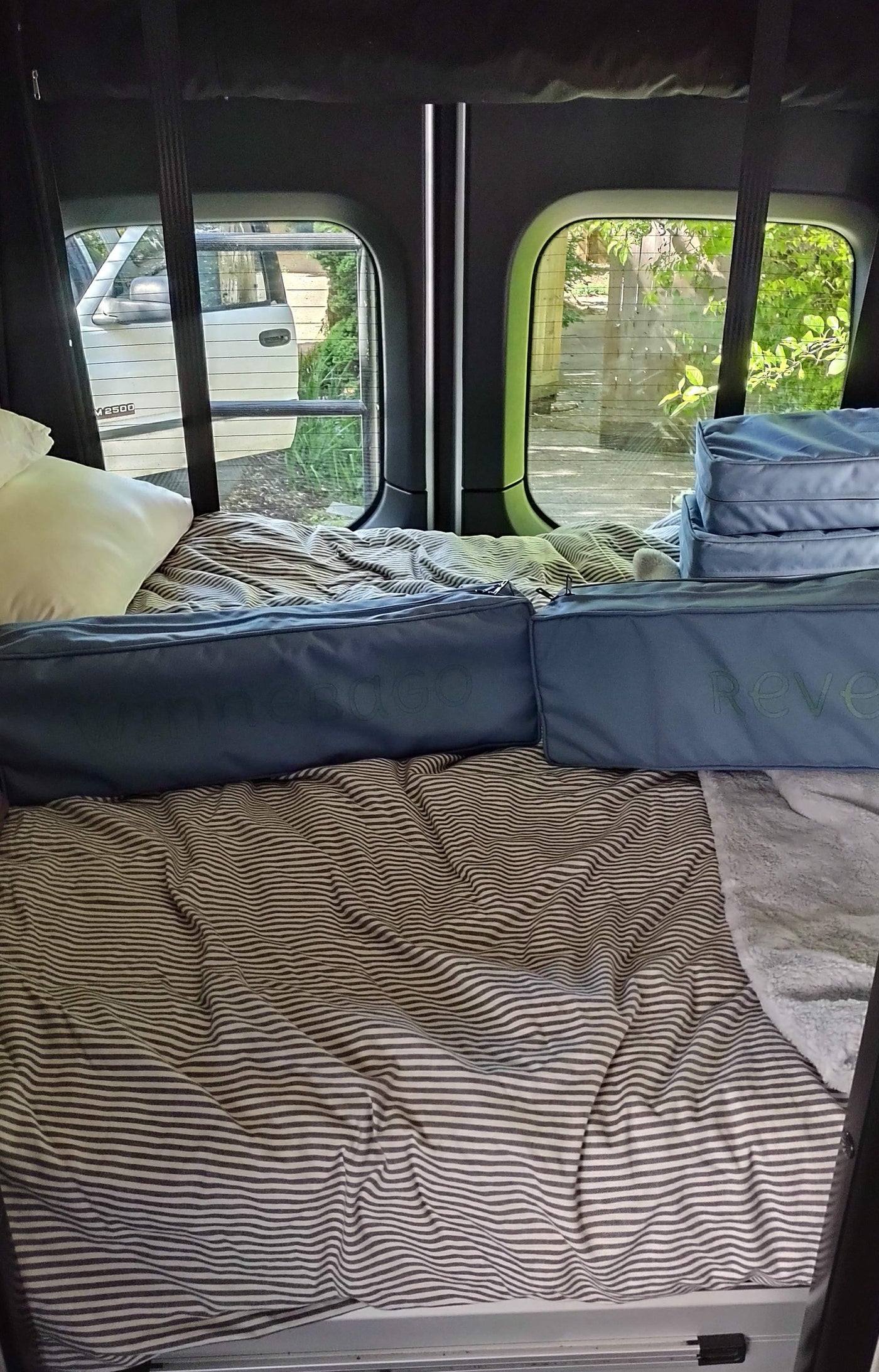 Revel RV rental interior: striped bed, pillow, and Omnesdo storage bags for a comfy journey. — photo 6