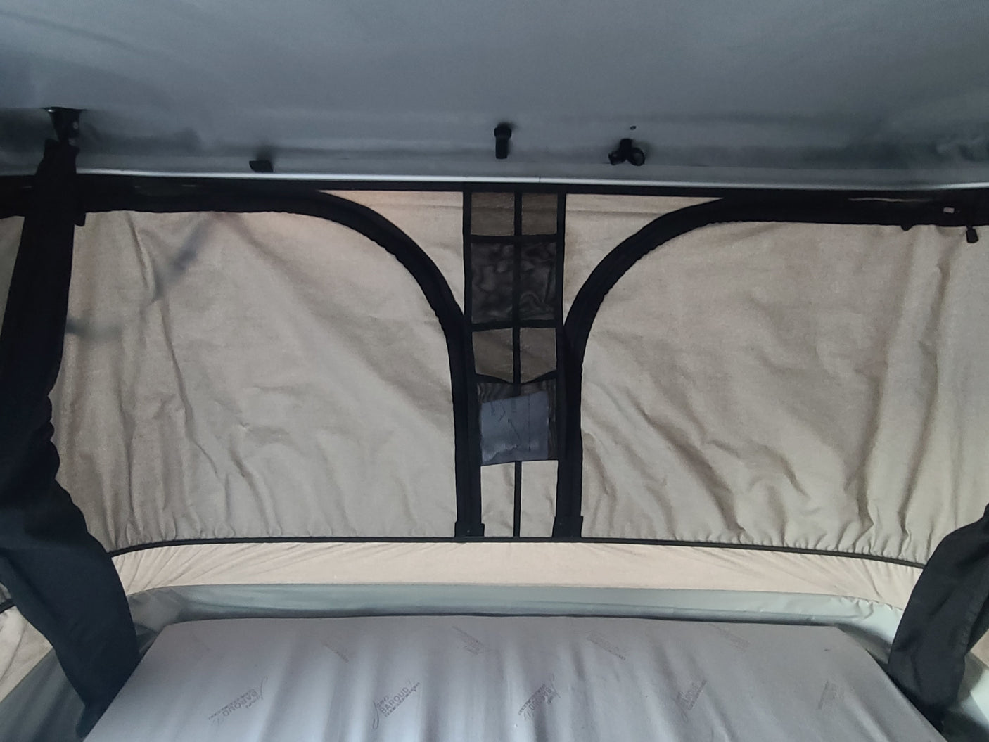 Inside an RV rental pop-top camper: a comfortable mattress and overhead mesh storage in the light-colored tent interior.
