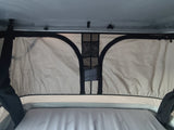 Inside an RV rental pop-top camper: a comfortable mattress and overhead mesh storage in the light-colored tent interior.