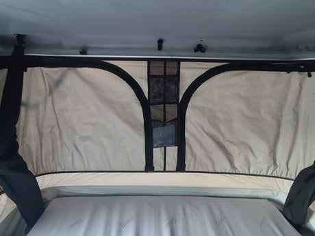 Inside an RV rental pop-top camper: a comfortable mattress and overhead mesh storage in the light-colored tent interior.
