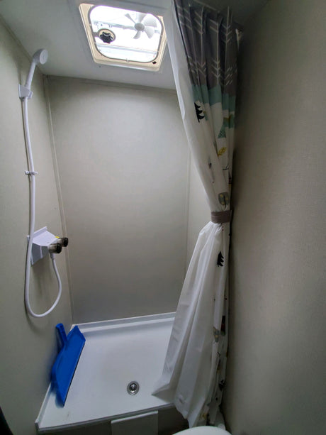 Compact RV rental shower with white pan, handheld showerhead, and a nature-themed curtain. Features a ceiling fan.
