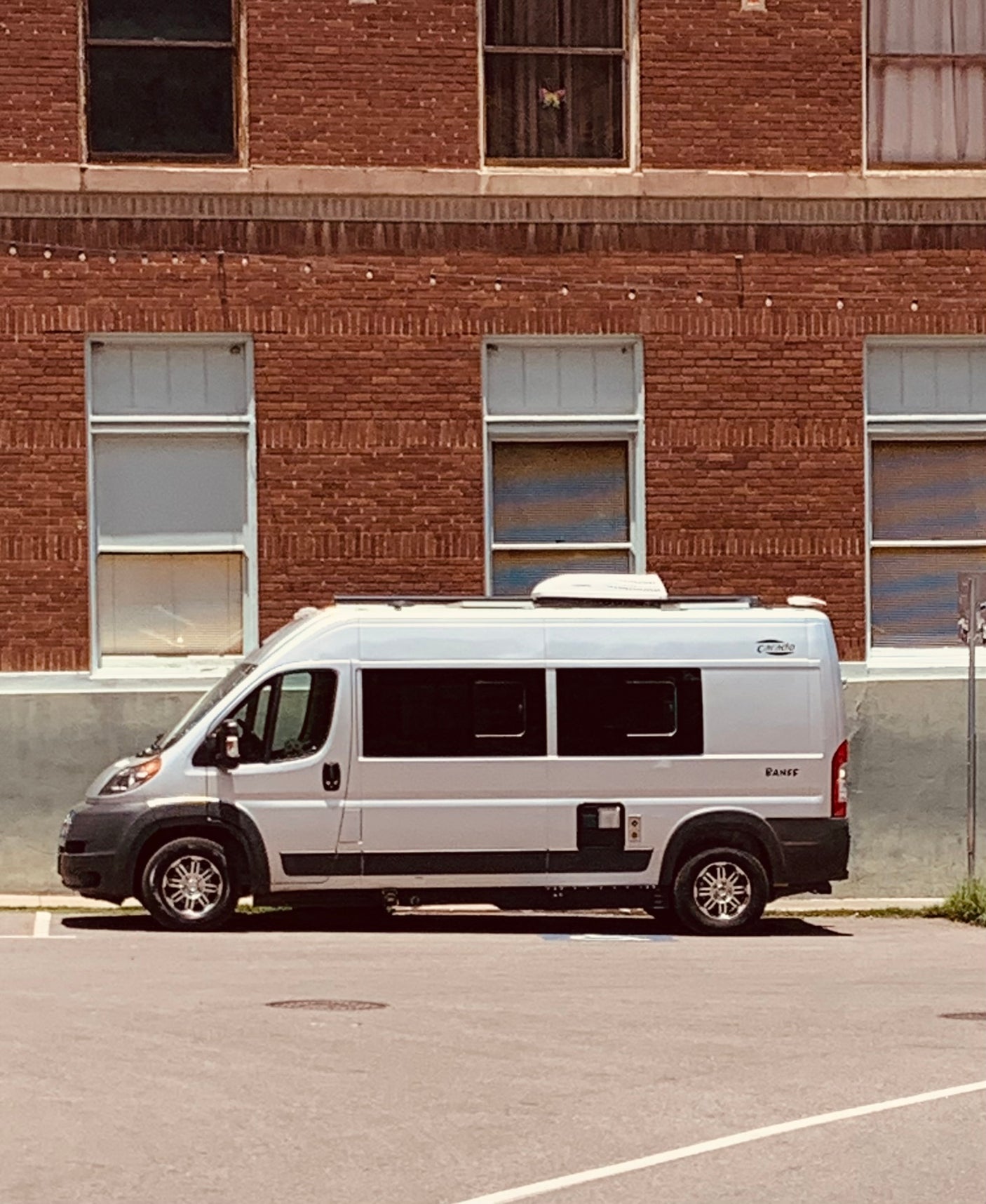 A white rv rental camper van is parked by a brick building, its compact size ready for travel adventures.