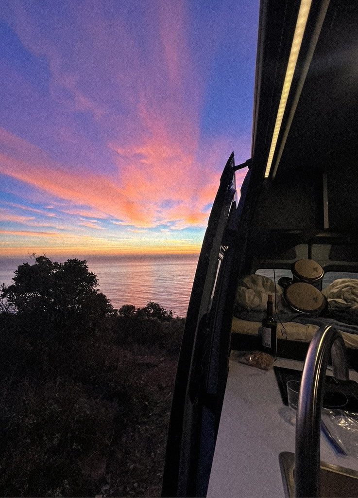 Coastal RV rental at sunset. View the vibrant sky and ocean from inside, featuring a sink, bed, and bongo drums. — photo 14
