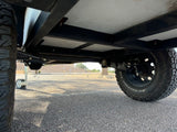 Underbody view of an off-road RV rental trailer, highlighting its robust chassis, suspension, and all-terrain tires.