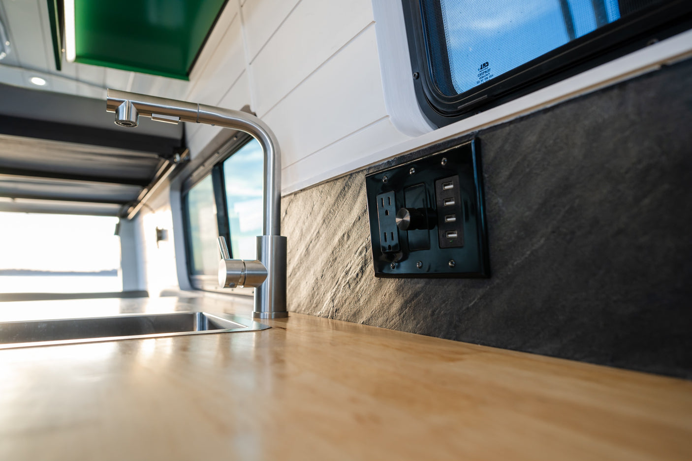 RV rental interior: A bright, modern kitchen features a stainless steel sink, wood counter, and outlets with USB and a dimmer knob.