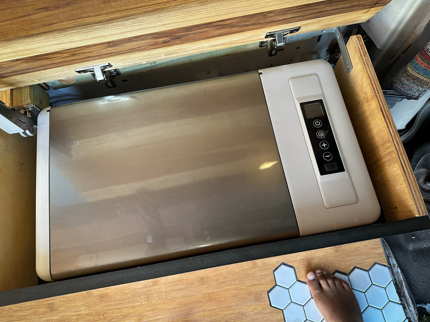 RV rental: Portable fridge with control panel nestled in a custom camper cabinet. Foot on hexagonal floor.
