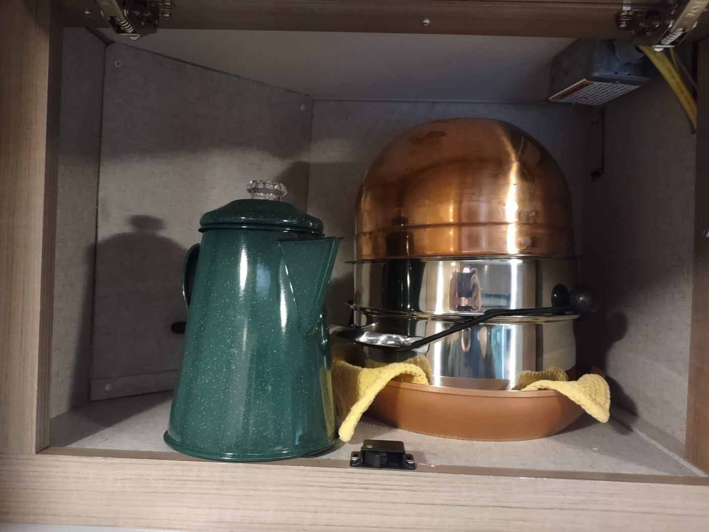 Inside an RV rental cabinet: A green coffee percolator and stacked cooking pots/pans for easy meals on the go.