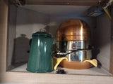 Inside an RV rental cabinet: A green coffee percolator and stacked cooking pots/pans for easy meals on the go.