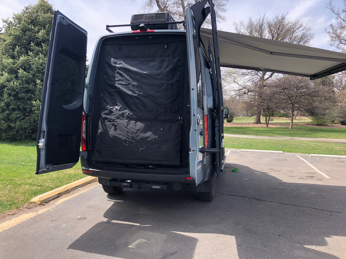 An RV rental camper van seen from behind, with its rear doors open, an interior panel visible, and a large side awning deployed. — photo 16